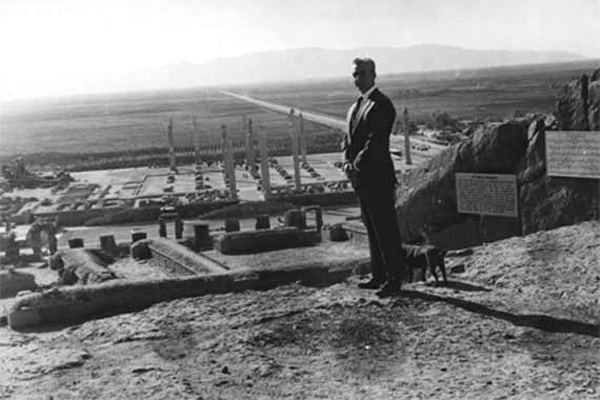محمد رضا شاه در تخت جمشید. وجه نمادین این عکس که گویی او بر بلندای تاریخ ایستاده و پشت به بزرگ ترین یادگار شاهان باستانی ایران داده، قابل تأمل است.